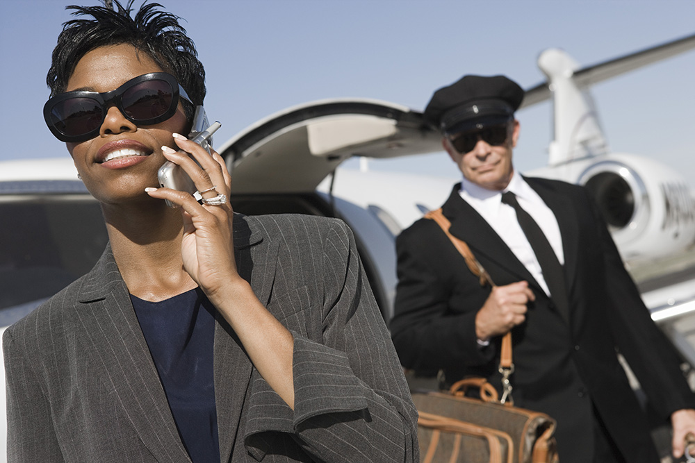 An African American business woman communicating on cell phone with security driver in the background at airfield